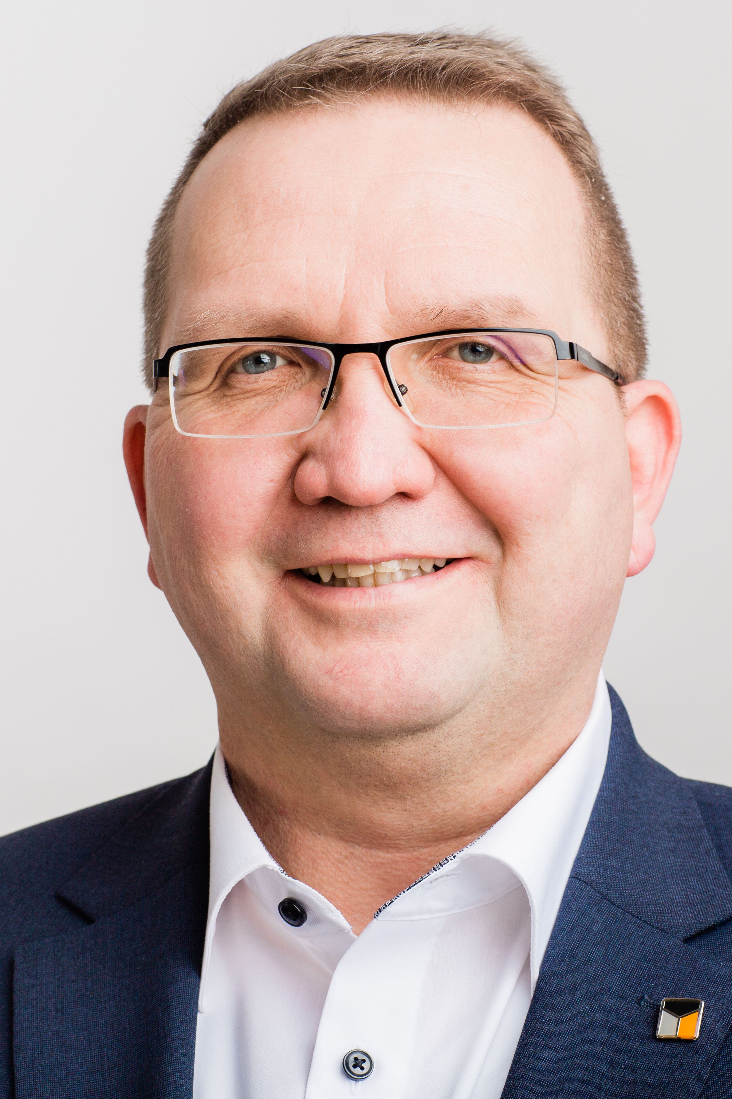 Ein Mann mit Brille, weißem Hemd und dunklem Sakko lächelt in die Kamera.